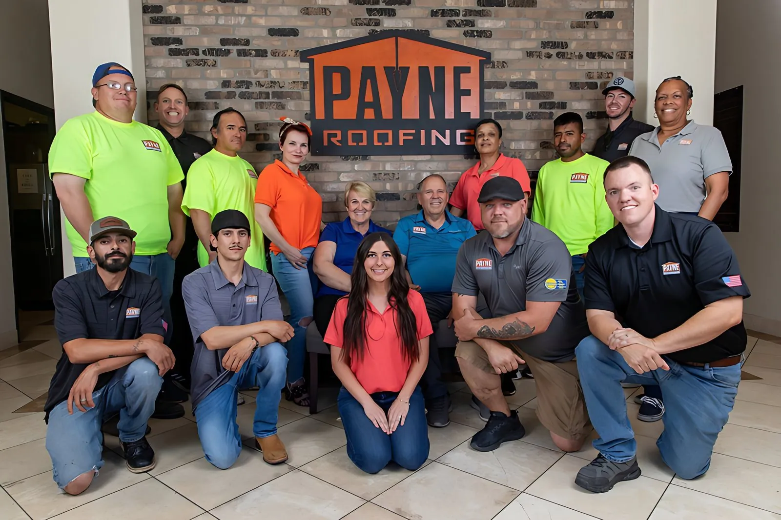The Payne Roofing team in front of the company logo